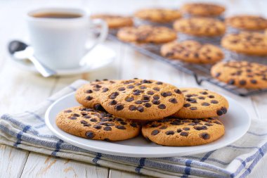 Çikolata parçalı lezzetli kurabiyeler ve açık mutfak masasında kahve, seçici bir odak..