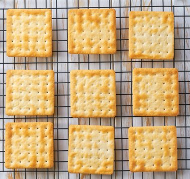 Tasty wheat water crackers cooling on a black wire rack, close up. Top view. clipart