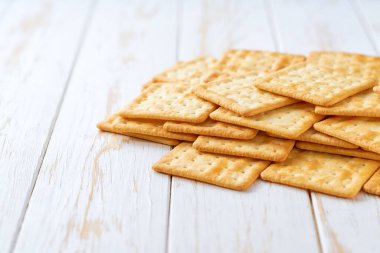 Pile of tasty wheat water crackers on a light kitchen table, with copy space for text. clipart