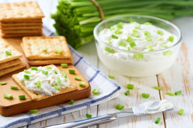 Cam kase krem peynir, taze soğan ve kraker, ahşap bir masada, seçici bir odak noktası..