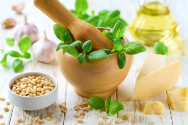 Beyaz ahşap bir masada İtalyan pesto sosu, çam fıstığı, sarımsak, zeytinyağı, parmesan ve yeşil fesleğen..