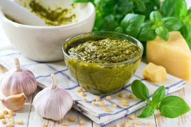 Beyaz ahşap bir masada İtalyan pesto sosu, çam fıstığı, sarımsak, zeytinyağı, parmesan ve yeşil fesleğen..