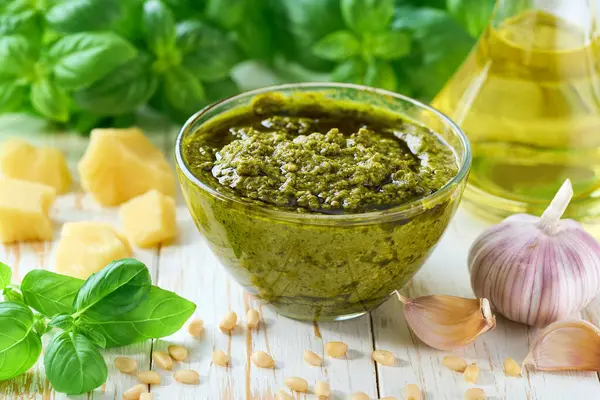 Mutfak masasında fesleğen yaprakları olan bir kasede geleneksel İtalyan soslu pesto. Ev yapımı İtalyan pesto sosu ve malzemeler. Geleneksel İtalyan sosu pesto.