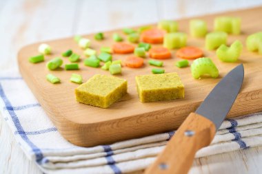 Kesme tahtasına havuç ve soğan konmuş Bouillon küpleri. Çorba hazırlamak için gerekli malzemeler.