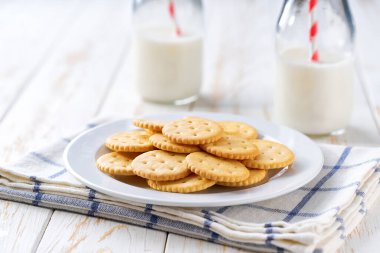 Taze süt ve tuzlu kraker dolu şişeler beyaz bir masada, seçici bir odak noktası..
