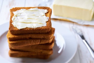 Beyaz bir masada tereyağlı ekmek dilimleri yığını..