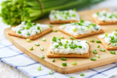 Süzme peynirli çıtır krakerler ve beyaz ahşap masada yeşil soğan..