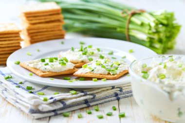Krem peynirli krakerler ve ahşap kesme tahtasının üzerinde yeşil soğan. Sağlıklı kahvaltı kavramı.