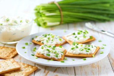Çıtır kraker, krem peynir ve ahşap bir masada yeşil soğan..