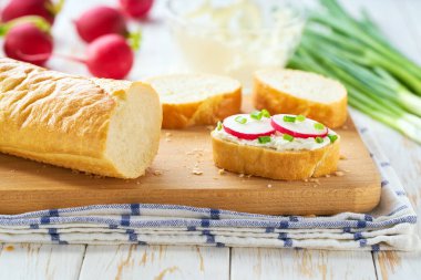 Hafif bir mutfak masasında yumuşak krem peynirli ve turplu baget kesmek. Lezzetli yaz atıştırmaları.