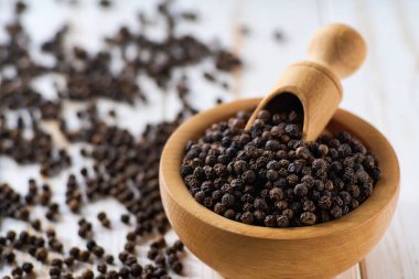 Beyaz ahşap bir masada siyah biberli ahşap kase, seçici bir odak..