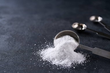 Bir çay kaşığından dökülen tuzlu su siyah bir taş masaya dökülmüş, seçici bir odak noktası..