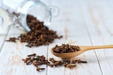 Ahşap kepçedeki karanfil ve beyaz ahşap masadaki cam saklama kavanozunda seçici bir odak noktası var..