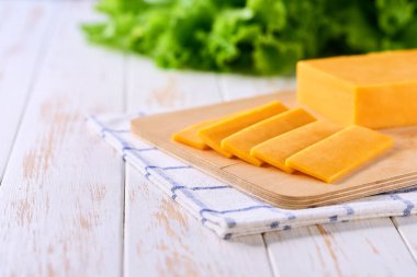 Beyaz ahşap bir masada kırmızı çedar peyniri parçaları, seçici bir odak.