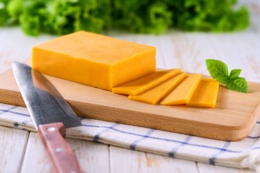 Beyaz ahşap bir masada kırmızı çedar peyniri parçaları, seçici bir odak.