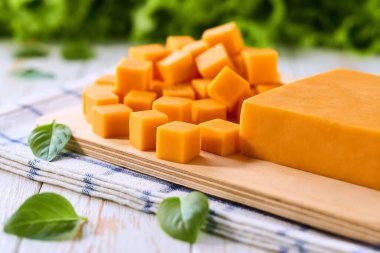 Beyaz bir mutfak masasında çedar peyniri küpleriyle tahta kesmek, seçici bir odak..