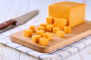 Çedar peyniri beyaz ahşap bir masada kesme tahtasının üzerinde küp şeklinde kesilmiş..