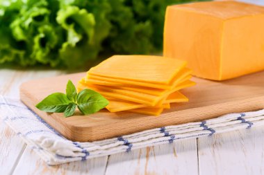 Beyaz ahşap bir masada dilimlenmiş doğal peynirli çedar peyniri, seçici bir odak..