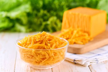 Açık mutfak masasında rendelenmiş çedar peynirli cam kase..