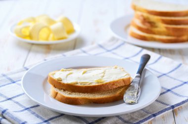 Beyaz ahşap bir masada buğday ekmeğine tereyağı sürüyorum..