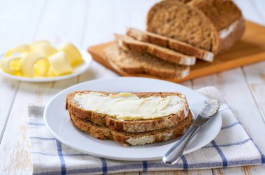 Hafif bir mutfak masasındaki çavdar ekmeğine tereyağı sürüyorum..