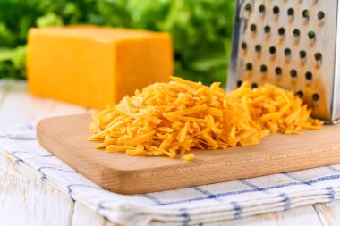 Beyaz ahşap bir masada rendelenmiş kırmızı çedar peyniri. Lezzetli çedar peyniri.