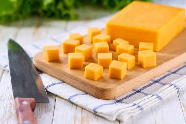 Beyaz ahşap masada çedar peyniri küpleri, seçici odak.