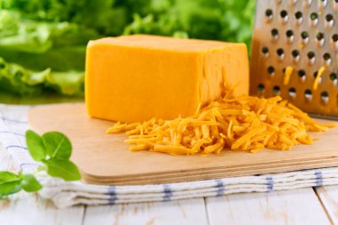 Beyaz ahşap bir masada rendelenmiş çedar peyniri, metin için kopyalama alanı.