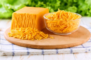 Açık mutfak masasında rendelenmiş çedar peynirli cam kase..