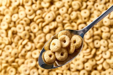 Arkaplan olarak lezzetli mısır gevreği halkalarının üzerine yulaf ezmesi bazlı yuvarlak mısır gevreği olan metal kaşık. Üst görünüm.