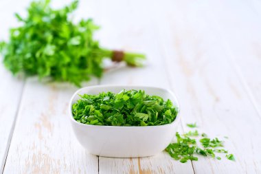 Aydınlık bir masada seramik tabakta doğranmış maydanoz, seçici bir odak..