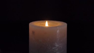 Büyük gri bir mumun alevi siyah bir arka planda izole bir şekilde yanıp sönüyor. Yavaş çekim, merkezi kare yakın çekim. 4k