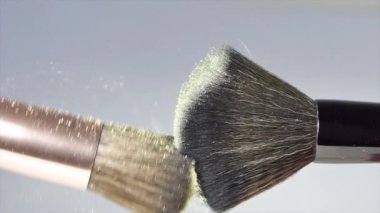 Makyaj fırçaları beyaz arka plan ve küçük kozmetik parçacıkları üzerinde birbirlerine dokunurlar