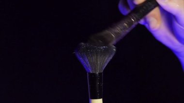 Makyaj fırçaları koyu arkaplan ve küçük kozmetik parçacıkları üzerinde birbirlerine dokunurlar