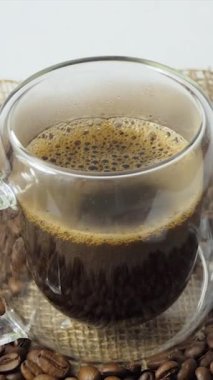 Taze kahve arkaplanlı bir fincan kahve. Şeffaf bir espresso fincanı ve arka planda bir yığın kavrulmuş kahve çekirdeği..