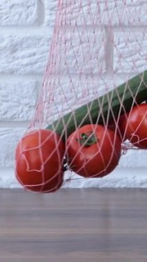 A woman takes out tomatoes and a cucumber from a reusable grocery bag vegetables on a table in the kitchen at home after shopping for groceries Waste-free and plastic-free concept. Mesh cotton shopper