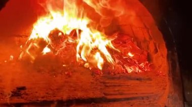 A fire is burning in a brick village stove. Flames, hot coals and logs close-up, close-up shooting. Chopped firewood burns in the furnace for cooking. 4k