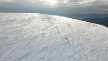 İki snowboardcu karla kaplı bir dağdan iniyor. İHA, alçalan snowboardcuların üzerinde uçuyor. Havadan çekilen 4K videosu, üst görüntü. Sıra dışı spor.