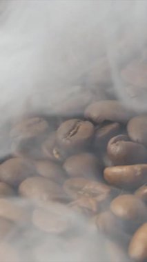 Kavrulmuş kahve çekirdeklerini yakından çek. Aromatik kahve çekirdekleri kahve çekirdeklerinden gelen kavrulmuş dumanlardır. Kızarmış tahıllar kahverengi bir torbanın üzerinde yatar. Ağır çekim. Döndürme kamerası.