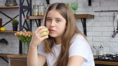 Healthy diet. Close up portrait of happy white girl biting and eating ripe green apple, looking at camera at kitchen interior 4K