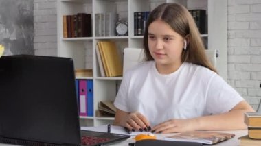 Kablosuz kulaklık takan genç bir kız öğrenci laptop mesafesinden evde öğrenim görüyor. İnternet kamerasında sohbet eden liseli kız çevrimiçi öğretmenle sınav ya da sınava hazırlanıyor. 4K