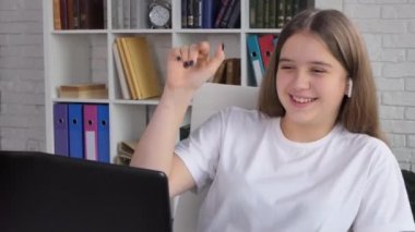 Kulaklık takan, el mesafesi yükselen, sanal ders sınıfında kameraya konuşan, evde video konferans görüşmeleri yapan sevimli bir kız öğrenci. 4k