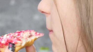 Close-up portrait: a happy beautiful young girl appetizingly bites a pink donut, licks her lips and laughs. The girl in the kitchen eats sweets cheerfully, happily.