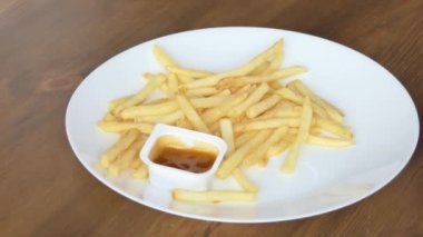 French fries on a white plate with sauce on a table in a cafe close-up. A company of friends eat potatoes close-up. 4K