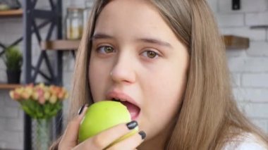 Healthy diet. Close up portrait of happy white girl biting and eating ripe green apple, looking at camera at kitchen interior 4K