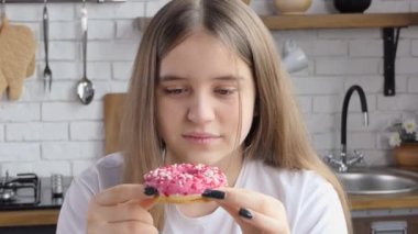 Uzun saçlı mutlu genç kız pembe çöreklerle oynayıp gülüyor. Mutfaktaki manken kız yüzünü buruşturuyor, seviniyor, gülümsüyor.