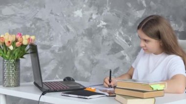 Uzaktan öğrenme konsepti. Ergenlik çağındaki liseli kız bilgisayarı kullanarak ders çalışıyor ve defterine not alıyor. Kulaklık takan genç bir kız öğrenci internet video kursu seyrediyor evde oturuyor.