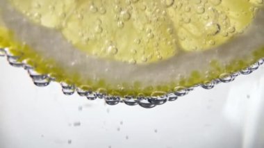 Slow Motion Macro shot of a lemon slice in water bubbles, Soft Drink with Ice, Bubbles, Mint and Lemon. Close Up Refreshment sparkles lemon soda and Cold Summer Drink 4K