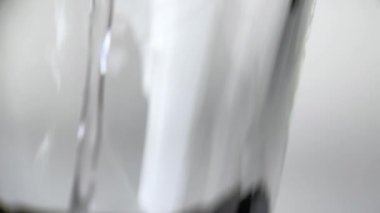 Yavaş çekimde su akışı pürüzsüz, temiz bir yüzeye düşer, hava kabarcıkları yaratır, düştükten sonra damlalar. Beyaz arka planda şeffaf bir kabın içine dökülen temiz mavi sıvının tazeliği.