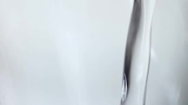 Yavaş çekimde su akışı pürüzsüz, temiz bir yüzeye düşer, hava kabarcıkları yaratır, düştükten sonra damlalar. Beyaz arka planda şeffaf bir kabın içine dökülen temiz mavi sıvının tazeliği.